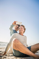 Father having fun with his son on the beach, taking smartphone pictures