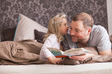 Father and daughter reading a book in bed, whispering in ear