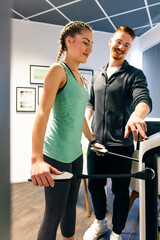 Young woman with personal trainer in fitness gym on body analysis device