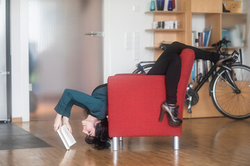Young woman reading a book, inverted on armchair