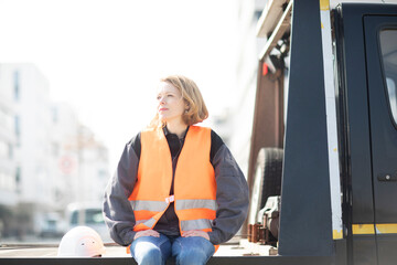 Woman wearing reflective vest sitting on truck platform