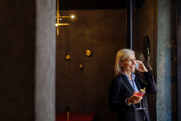 Mature businesswoman taking after work cocktail, talking on the phone