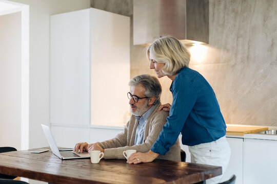 Mature man with wife using laptop on kitchen table at home