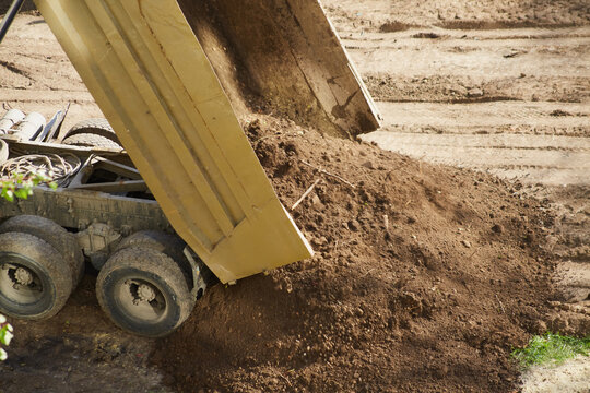 The truck's bed tips to release a load of soil, close-up,  earth pouring out from the truck bed