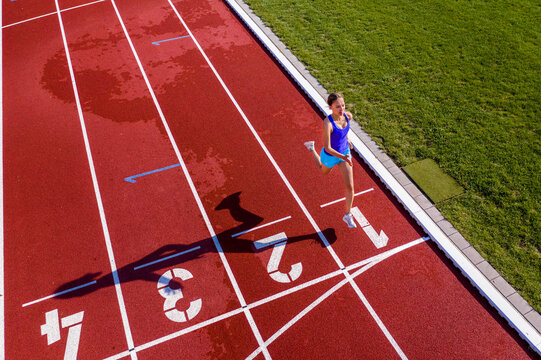 Aerial view of a running young female athlete on a tartan track crossing finishing line