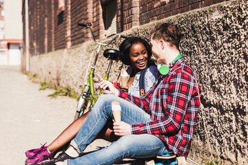 Young couple sitting on ground, eating icecream