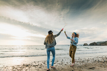 Happy friends making soap bubbles on the beach