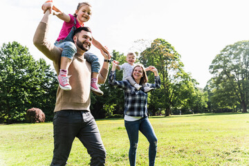 Happy parents carrying children on shoulders in a park