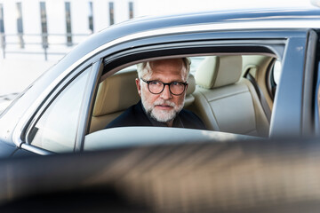 Mature businessman sitting on backseat in car, looking out of window
