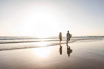 Young couple running on beach, carrying surfboard