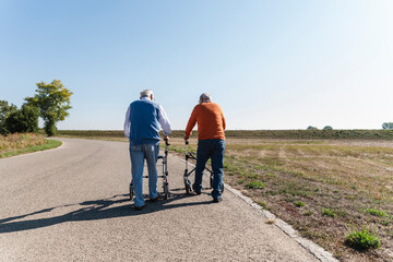 Two old friends walking on a country road, using wheeled walkers