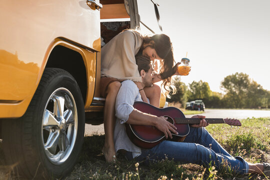 Affectionate couple on a road trip, taking a break, kissing, playing guitar