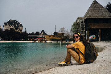 A young woman travels with one backpack. A girl with dreadlocks sits near a turquoise lake and...