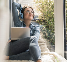 Woman with headphones and laptop sitting at the window at home