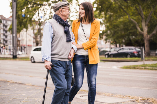 Adult granddaughter assisting her grandfather strolling with walking stick
