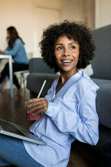 Happy woman with soft drink sitting on floor using laptop