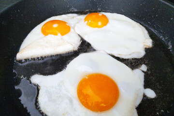 Close-Up of Three Sunny-Side-Up Eggs Frying in a Pan - Breakfast Food Concept for Kitchen, Cooking, and Recipe Design