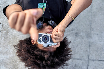 Young man laying on wall and taking pictures with his camera and pointing with his finger