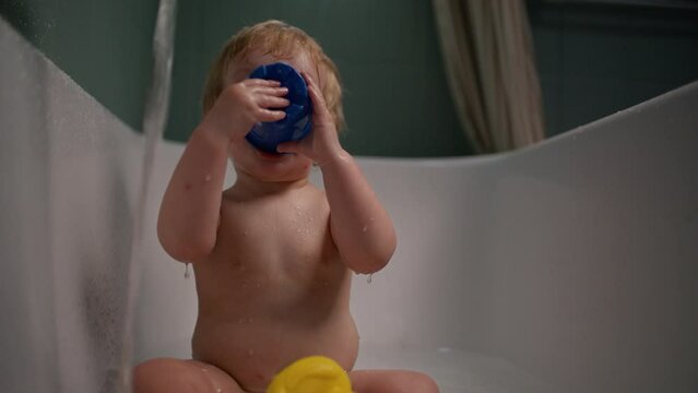 Adorable Baby In Bathtub Plays With Blue Toy Bucket
