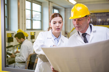 Two engineers in factory looking at plan