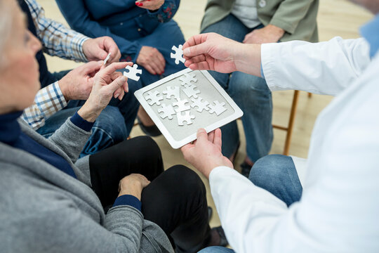 Doctor playing jigsaw puzzle with group of seniors in retirement home - Powered by Adobe
