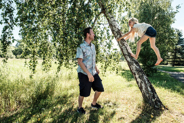 Father watching daughter climbing a birch trunk in park