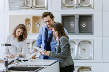 Customers consulting saleswoman in shop for kitchen sinks