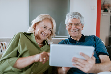 Happy senior couple at home sitting on couch sharing tablet