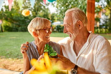 Happy senior couple clinking beer bottles on a garden party