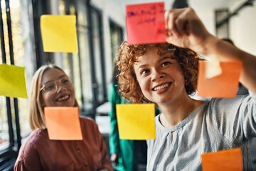 Happy colleagues with sticky notes at glass pane in office
