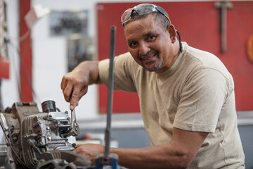 Smiling mechanic working on motorcycle engine in workshop