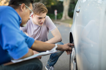Learner driver with instructor checking tyre of a car