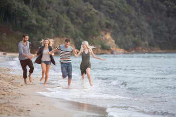 Four happy friends running at the beach