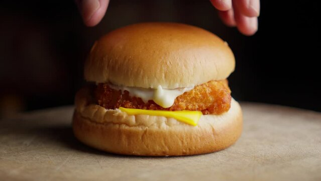 Putting Bun On Fried Fish Burger Spread With Mayonnaise And Cheese. Close-up Shot