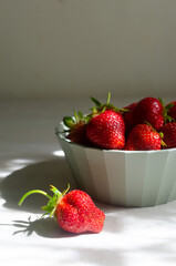 Ripe red strawberries in a green bowl on a gray table. Concept of summer food. Vertical orientation. Selective focus. Hard light. Copy space