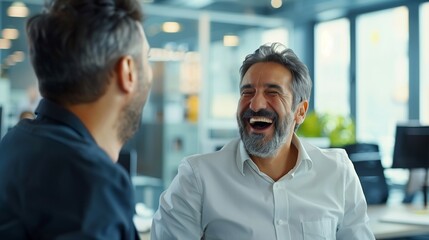 A bank manager laughing and enjoying a casual conversation with a colleague in his well-organized office.