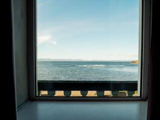 A window with a curtain is open with view of the ocean. The scene is of the water and the sky. Bundoran area, Ireland. Warm sunny day. Blue sky. Popular travel area and resort.