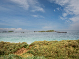 Tall green grass on a sand dune and amazing tropical blue color ocean water and blue cloudy sky. Stunning Glassilaun Beach in Connemara, Ireland. Travel and tourism. Nobody.