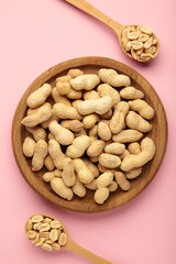 Fresh healthy peanuts in bowl and spoon on pink background.