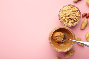 Jar and spoon of peanut butter on pink background.