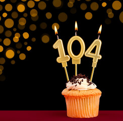 Number 104 birthday candle - Cupcake on black background with out of focus lights