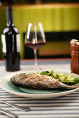 Grilled dorado fish served with vegetables and red wine in the background. Luxurious Italian restaurant