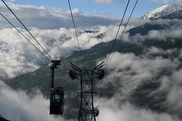 Gondola lift descending mountain with view of clouds below