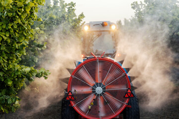 Agricultural machine on tractor driving through orchard and spraying with fertilizer