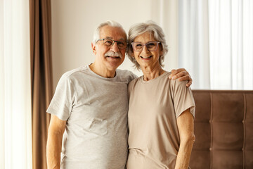 Portrait of a happy senior couple in love standing in a bedroom at home and hugging.