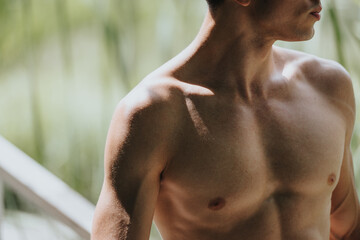 Close-up of shirtless young man with defined muscles highlighting fitness and health, captured in...