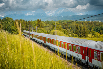Modern electric passenger train enters the train station. Beautiful montains landscape in background.