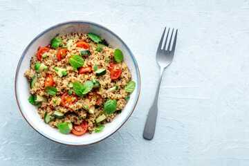 Quinoa tabbouleh salad in a bowl, a healthy dinner with tomatoes and mint, with a fork, top shot with copy space