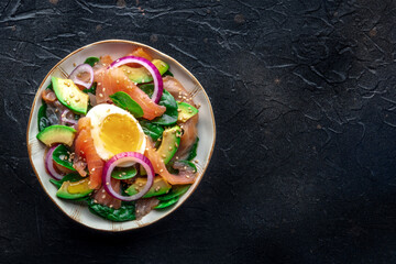 Salmon, avocado and egg salad with fresh leaves and onions, overhead flat lay shot on a black slate background. Healthy diet, with copy space