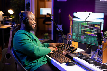 Young musician twisting knobs and mixing tunes with a console, following record settings on a digital software interface. Artist composer producing new music hits in his home studio.